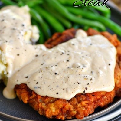 a plate with chicken fried steak topped with gravy and mashed potatoes and green beans also on the plate.