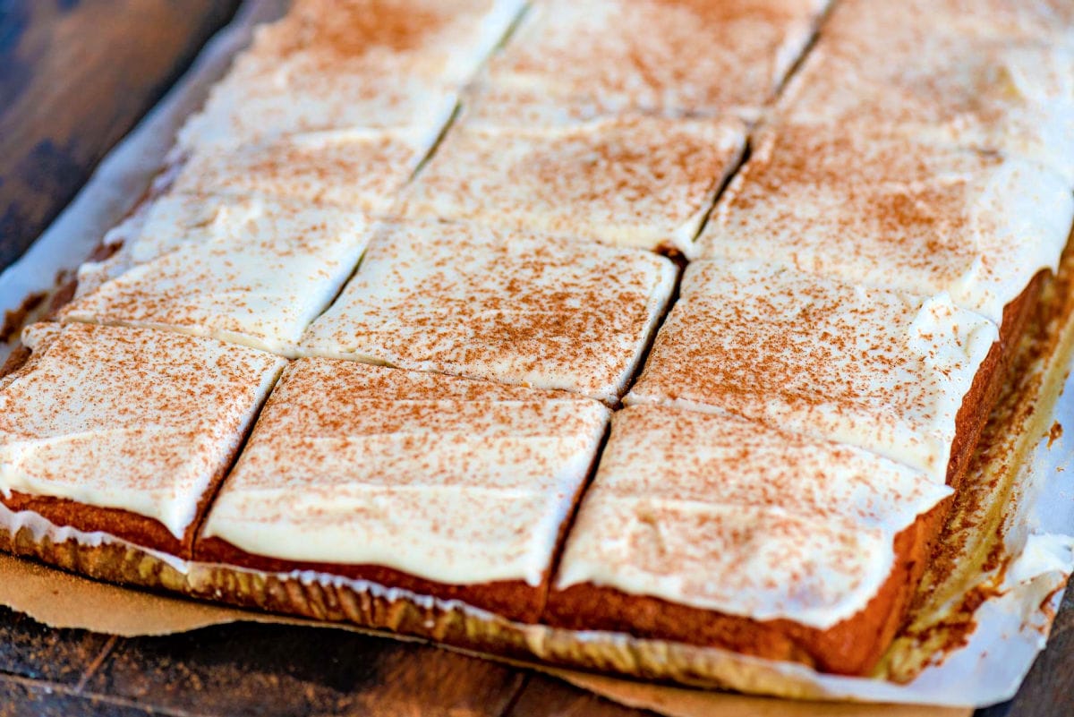 pumpkin bars frosting with cream cheese frosting and sprinkled with pumpkin pie spice. the bars have already been cut into squares and are ready to serve.