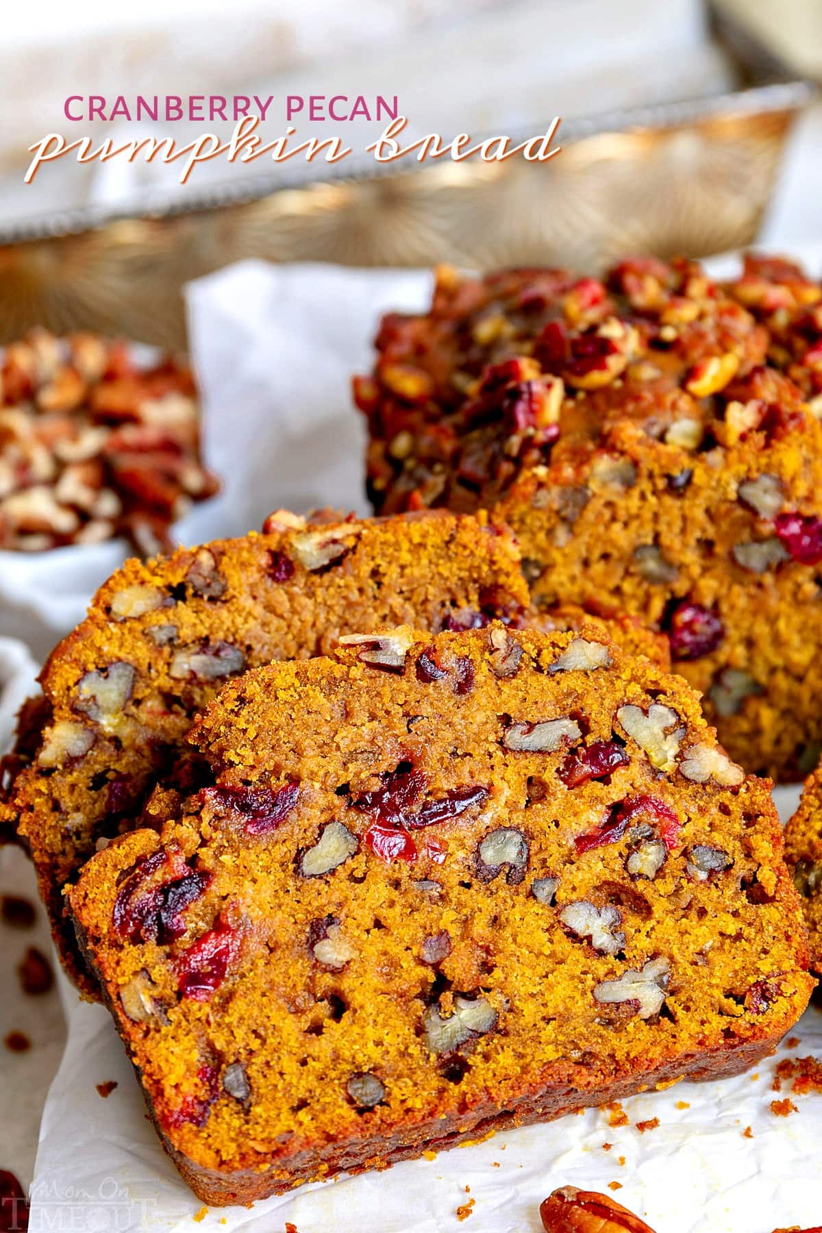 two slices of pumpkin bread made with dried cranberries and pecans sitting next to the rest of the loaf.