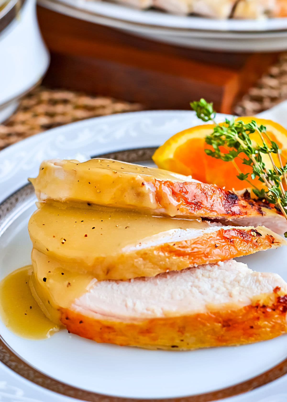 three slices of turkey breast topped with a silky smooth brown turkey gravy sitting on a white china plate with border.