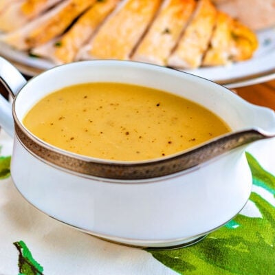 gravy boat filled to the top with turkey gravy. turkey carved in background.