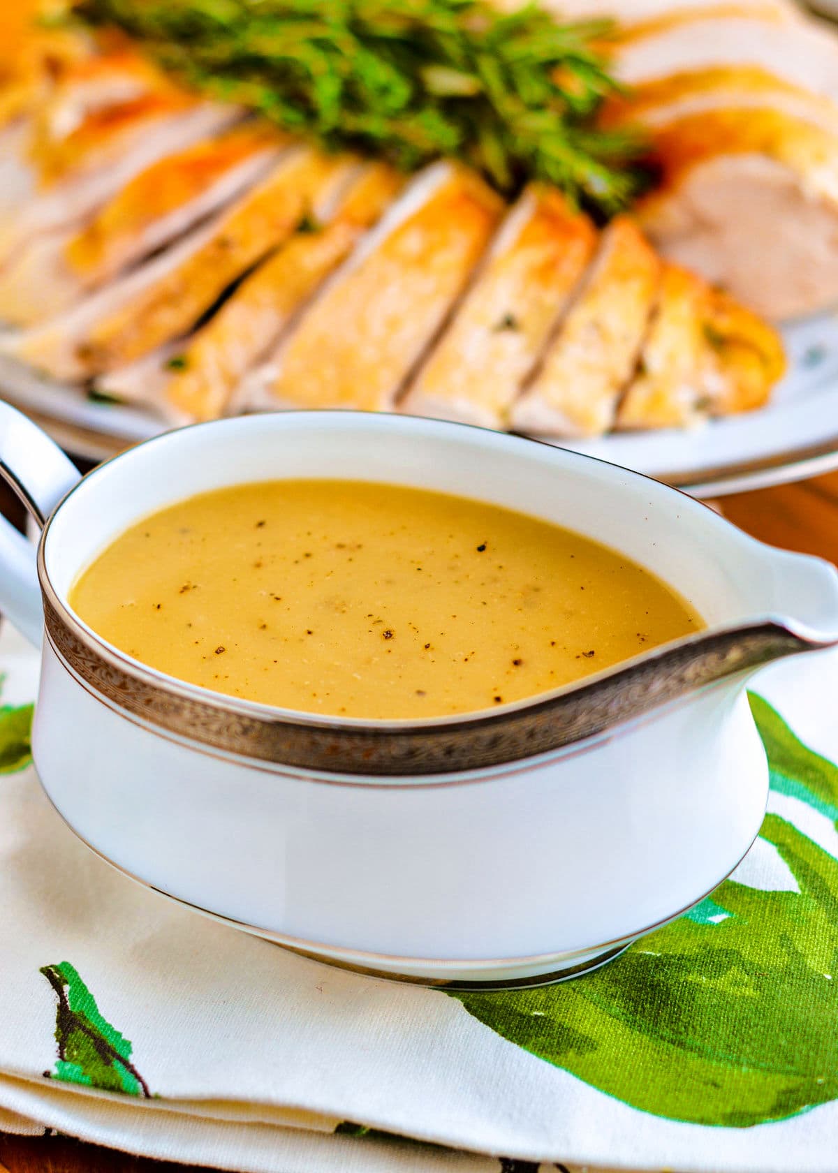 gravy boat filled to the top with turkey gravy. turkey carved in background.