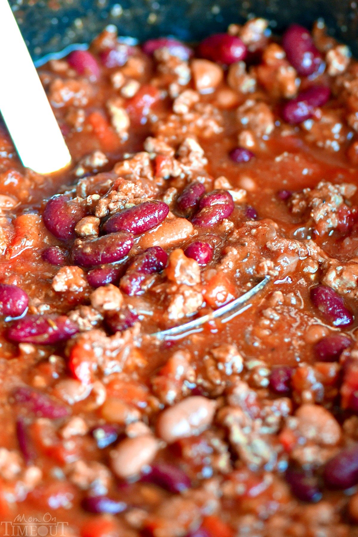 chili sitting in in black slow cooker with a stainless steel ladle resting in the insert.