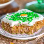 Carrot cake bar on white round plate with bite taken. Cream cheese frosting on top with green sprinkles.