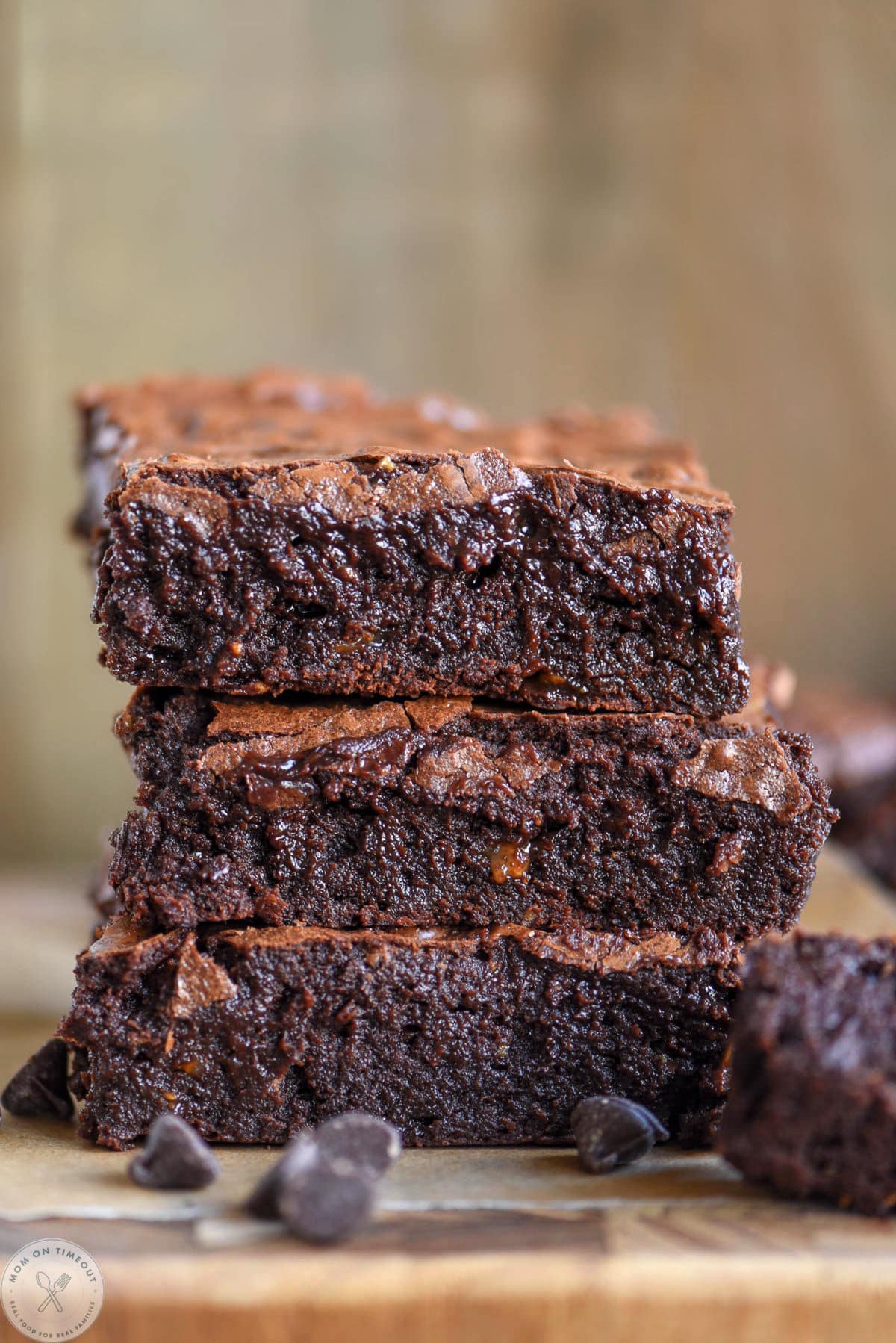 Three flourless brownies stacked on each other on wood cutting board.