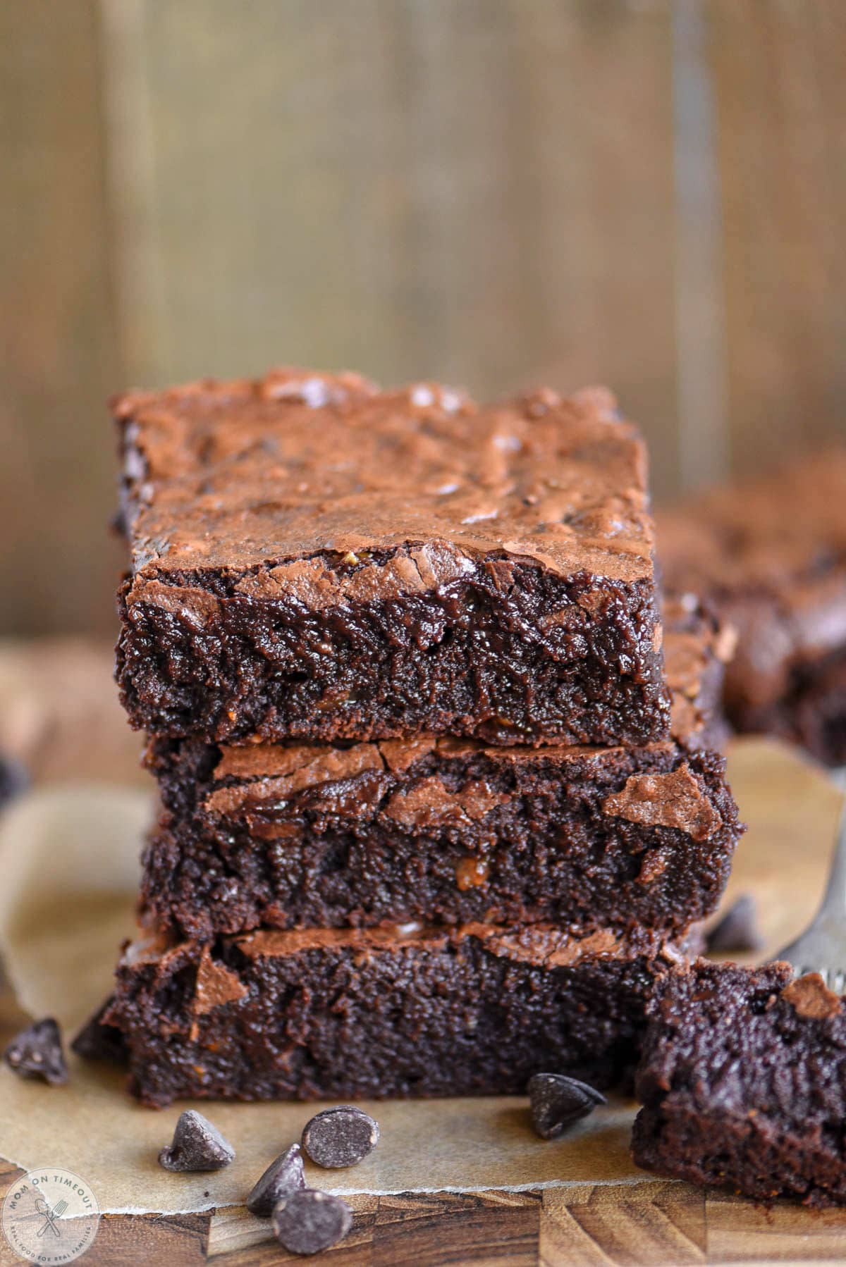Three flourless brownies stacked on each other on wood cutting board.