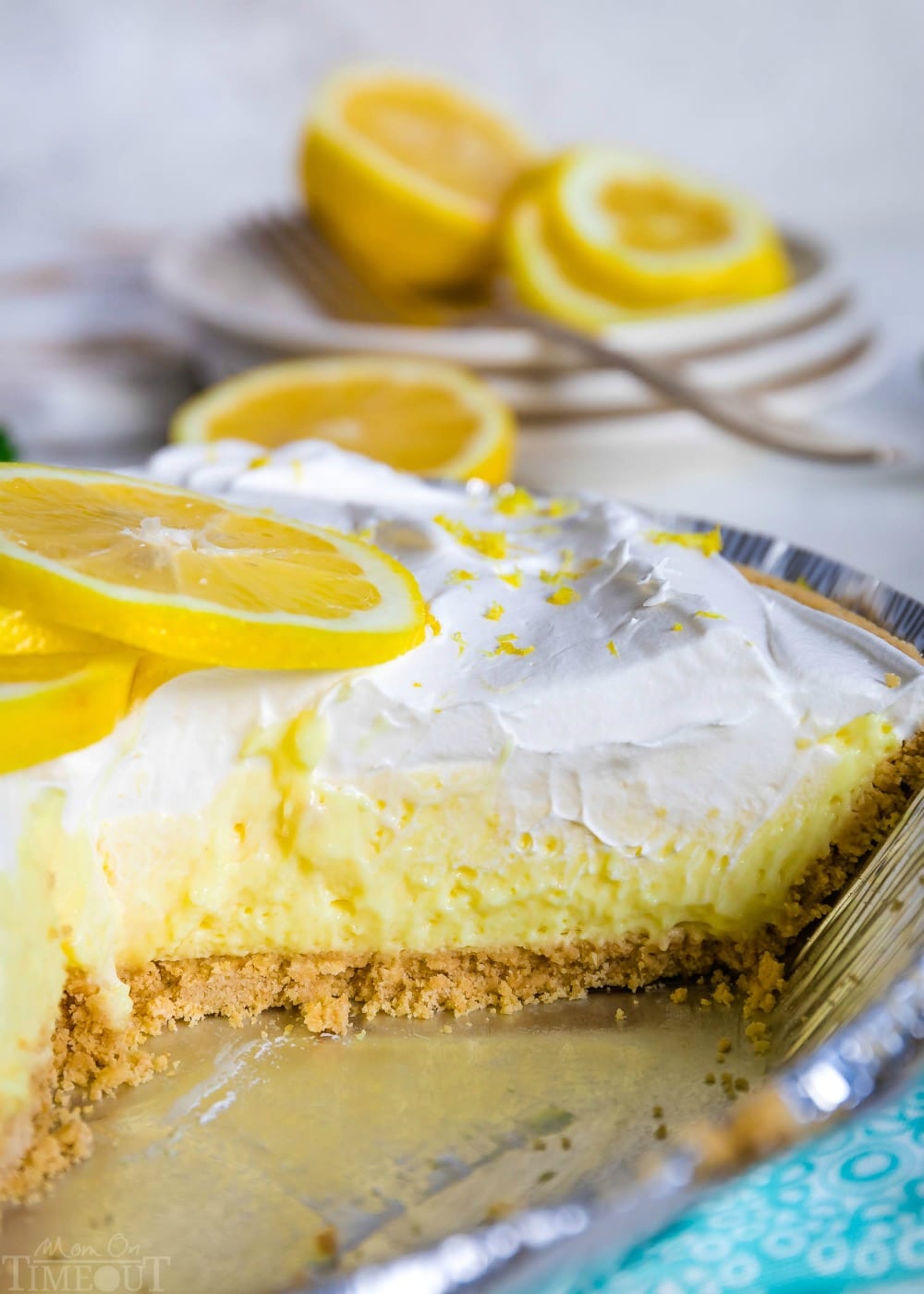 This easy No Bake Lemon Pie is perfect for hot summer days! Loaded with tart lemon flavor, the creamy lemon filling goes perfectly with the graham cracker crust and fresh whipped cream topping. Delicious! // Mom On Timeout #lemonpie #lemonpierecipe #nobakelemonpie #nobake #dessert #lemon #desserts #summer #lemon #grahamcrackercrust lemon pie in pie tin with a slice removed.