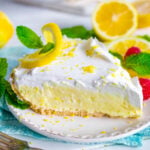 lemon pie topped with whipped cream on white plate with sliced lemons in background.