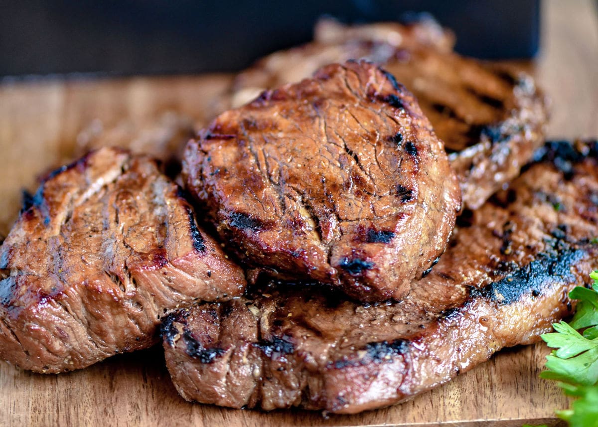 cooked steaks with lovely grill marks on wood cutting board ready to be sliced and served.