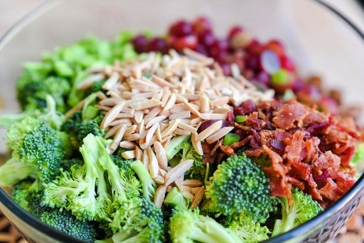 clear glass bowl filled with broccoli salad ingredients ready to be tossed together with the broccoli salad dressing.