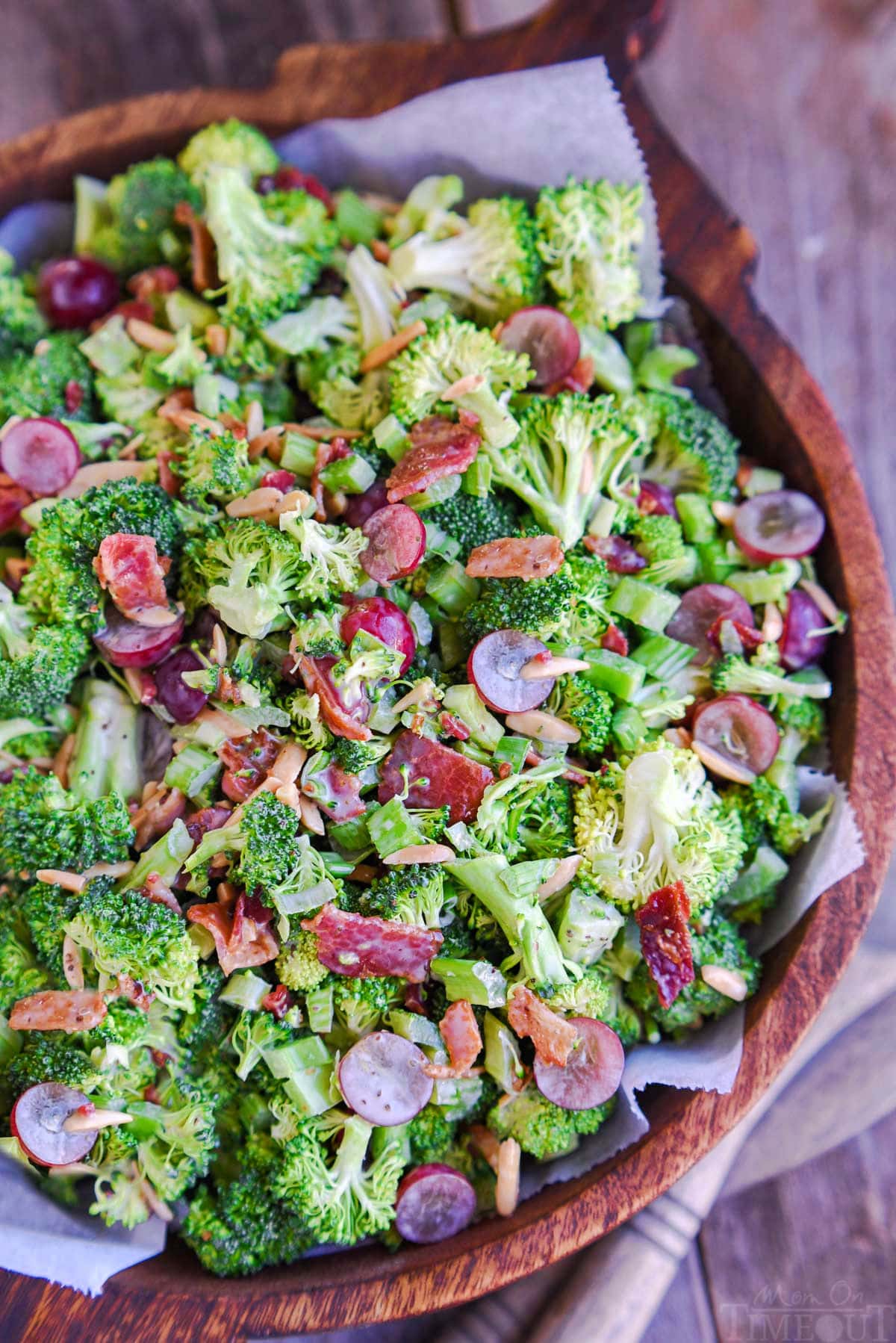 top down view of broccoli salad with bacon in a large wood bowl. Red grapes and toasted almonds can be seen tossed in the salad.