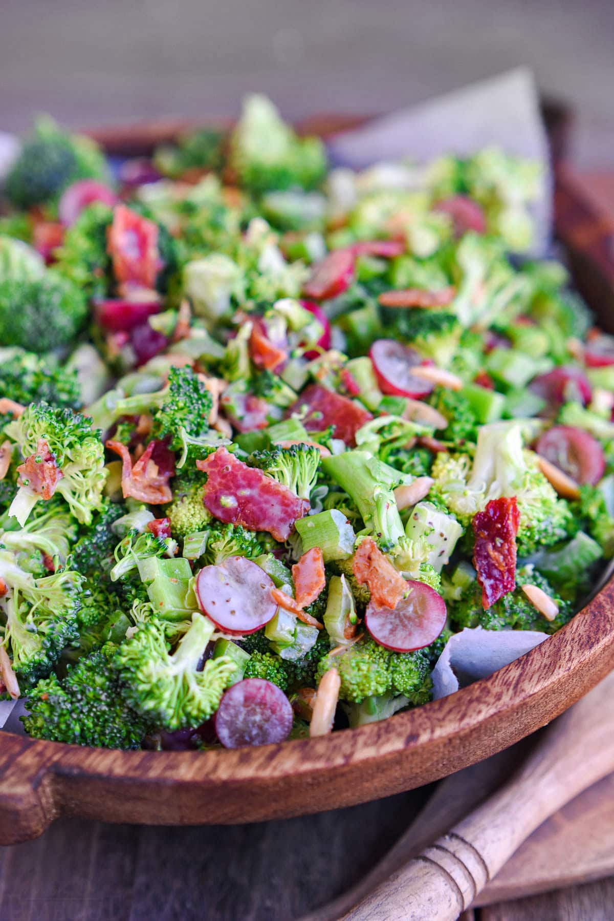 dark brown wood bowl filled with freshly prepare broccoli salad recipe made with grapes and bacon. 
