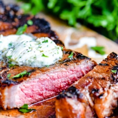 steak on cutting board with compound butter melting on top. one piece cut off of steak with fresh parsley in the background.