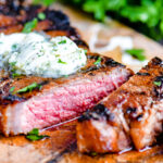 steak on cutting board with compound butter melting on top. one piece cut off of steak with fresh parsley in the background.