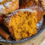 Close up shot of half a pumpkin muffin sitting on metal plate with more muffins behind it.