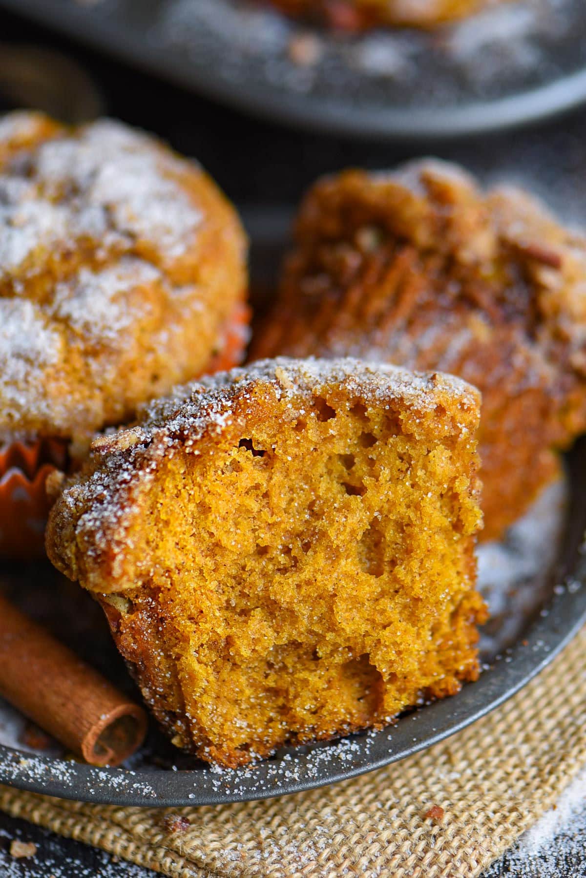 Close up shot of half a pumpkin muffin sitting on metal plate with more muffins behind it.
