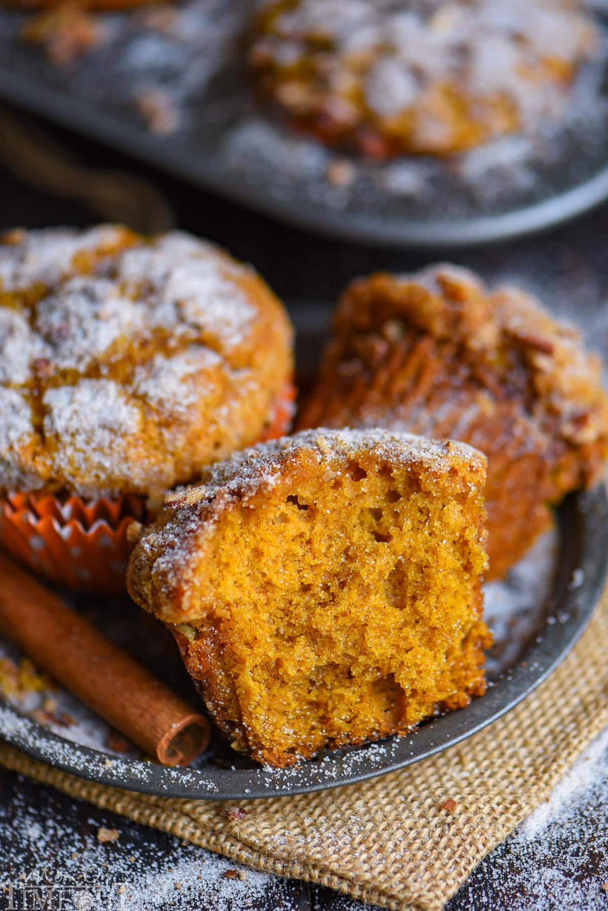 Three pumpkin muffins sitting on metal plate with cinnamon sticks next to them.