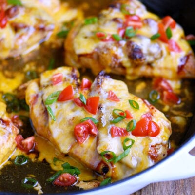 four servings of monterey chicken still in the skillet with diced tomatoes and green onions scattered on top for garnish.