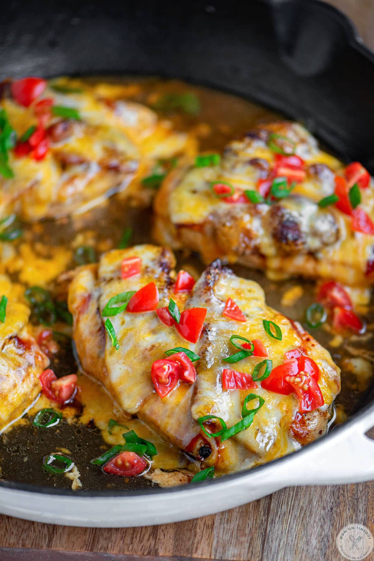 Close up angled shot of monterey chicken in skillet garnished with green onions and tomatoes ready to enjoy.
