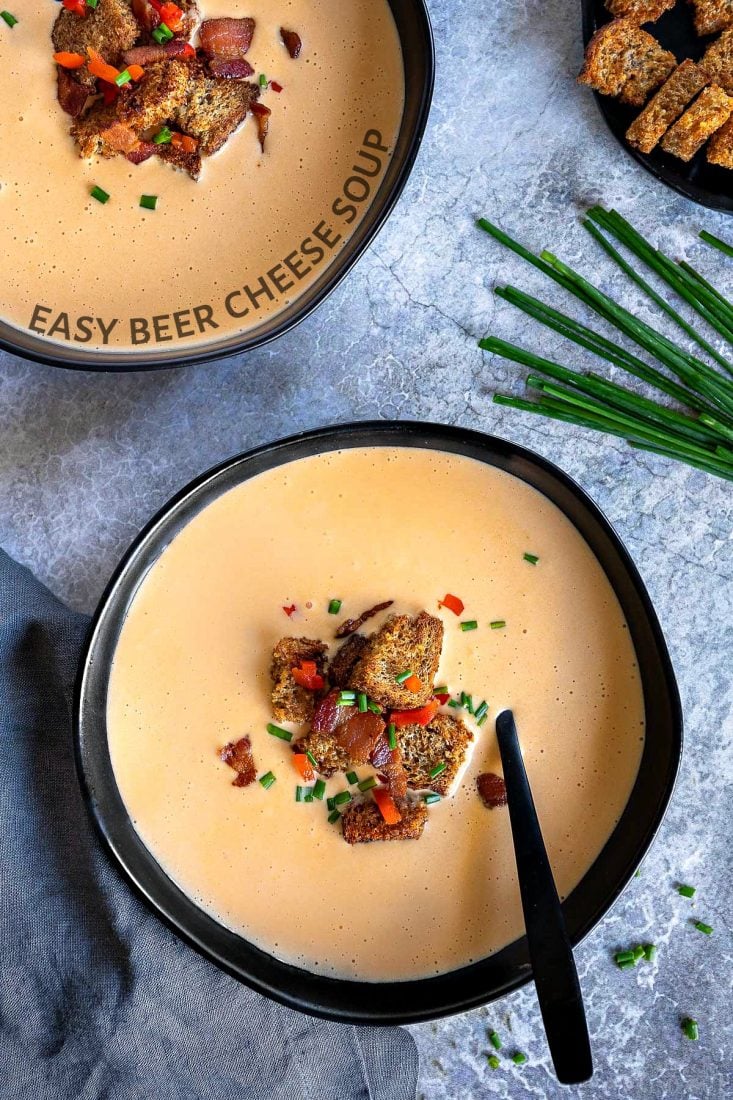 beer cheese soup recipe in black bowls with croutons bacon and chives text
