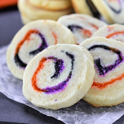 Halloween Sugar Cookies made with orange, black and purple sugar rolleed into a spiral. A stack of cookies in the back and five cookies fanned out in the front to showcase the neat spiral design.