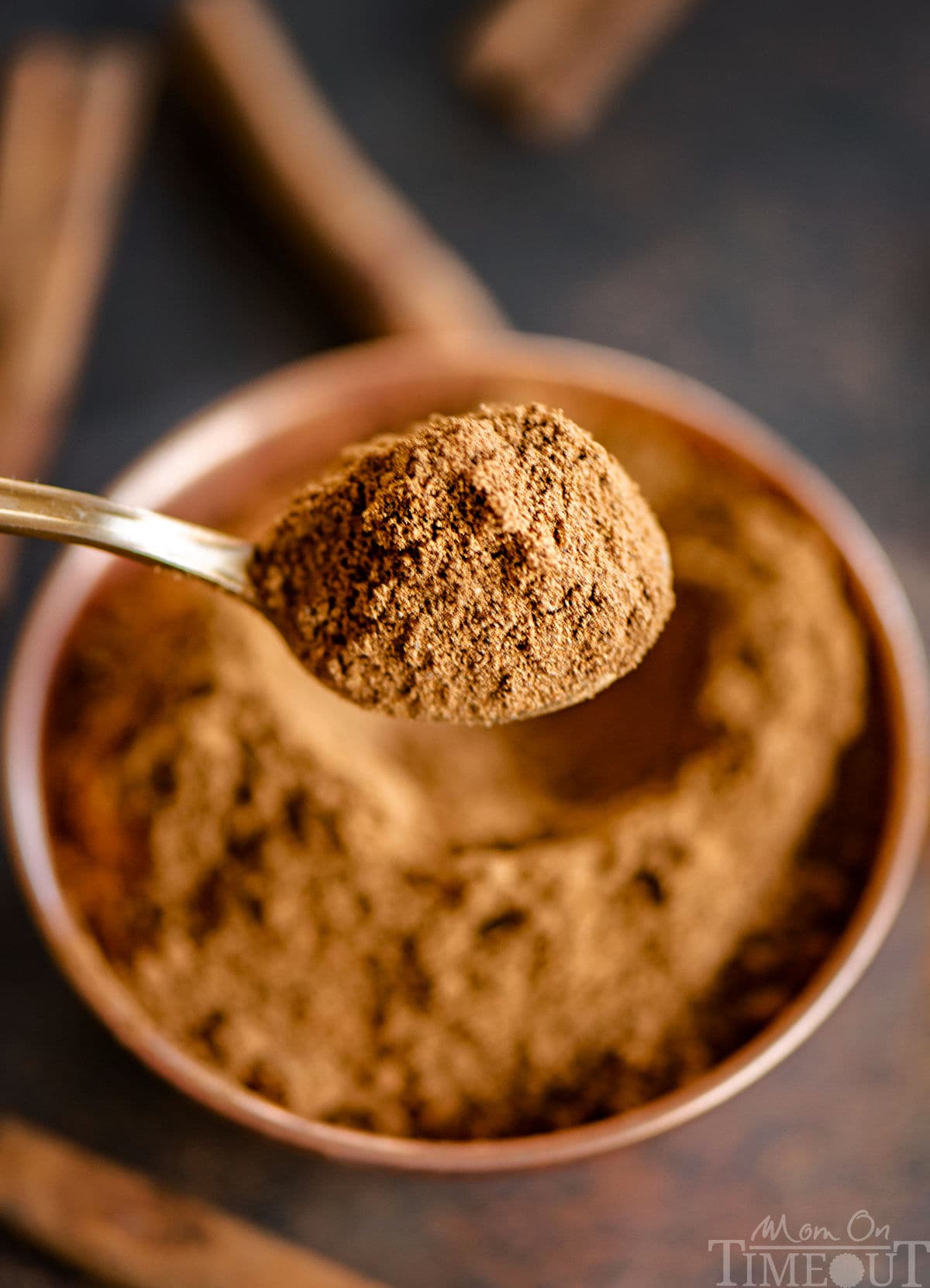 Spoonful of pumpkin pie spice held up over bowl where five spices were mixed together.