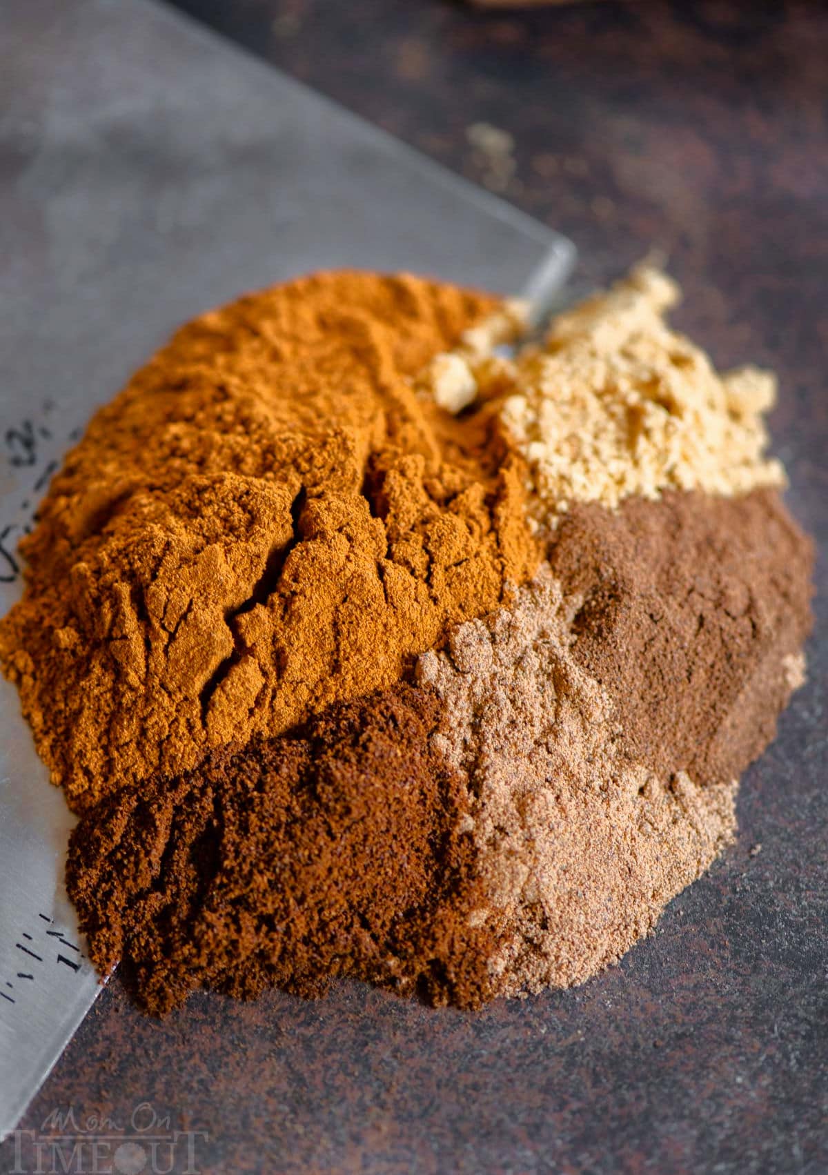 Pumpkin pie spice recipe ingredients being bench scraped off a surface ready to be mixed together and placed in an airtight jar.