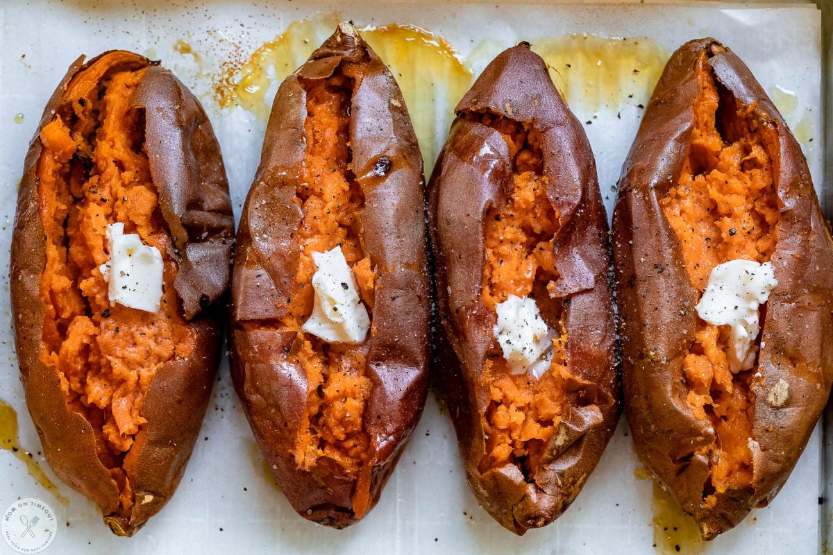 Four baked sweet potatoes on parchment lined baking sheet baked, cut open and ready to eat.