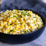 black bowl of creamed corn with chives snipped on top.