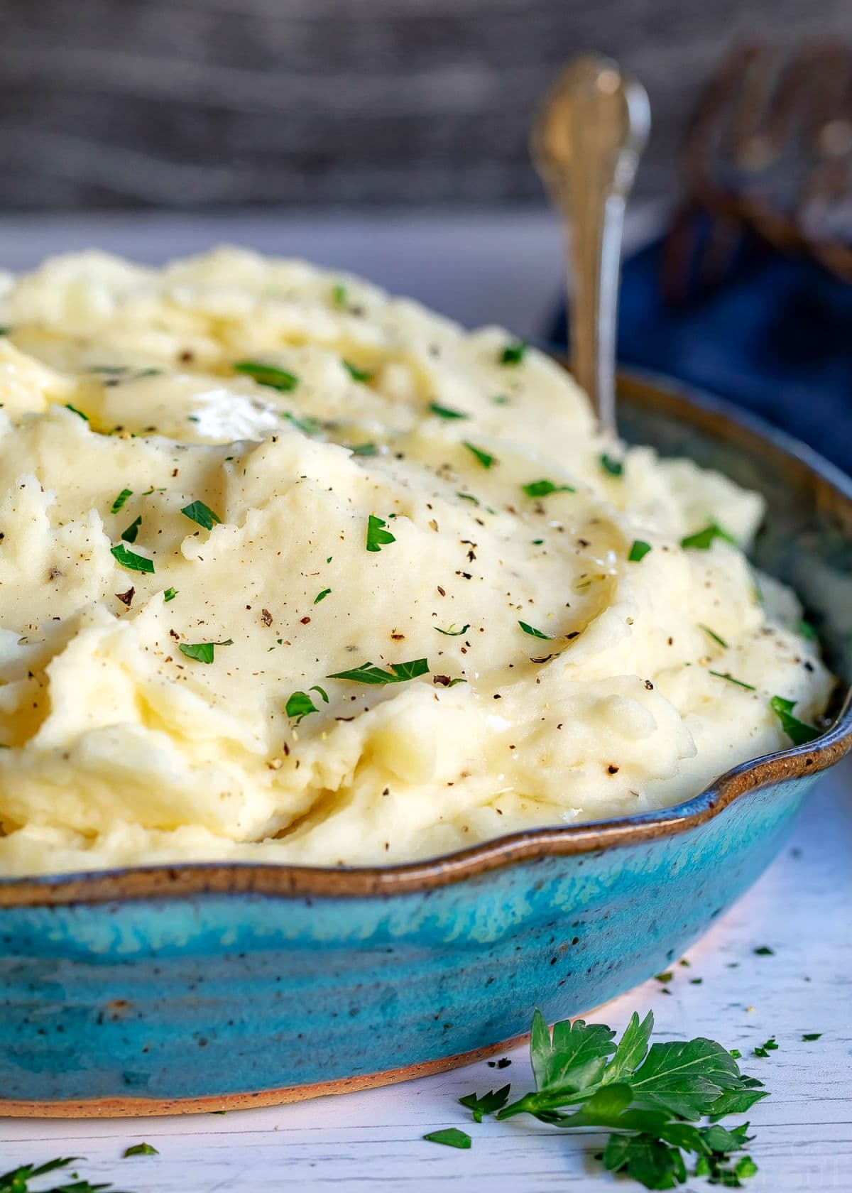 homemade mashed potatoes recipe in serving dish with spoon and chopped parsley sprinkled on top