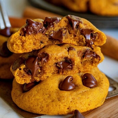 two pumpkin chocolate chip cookies with one of them split in half and stacked on the other. Chocolate chips are still melty.