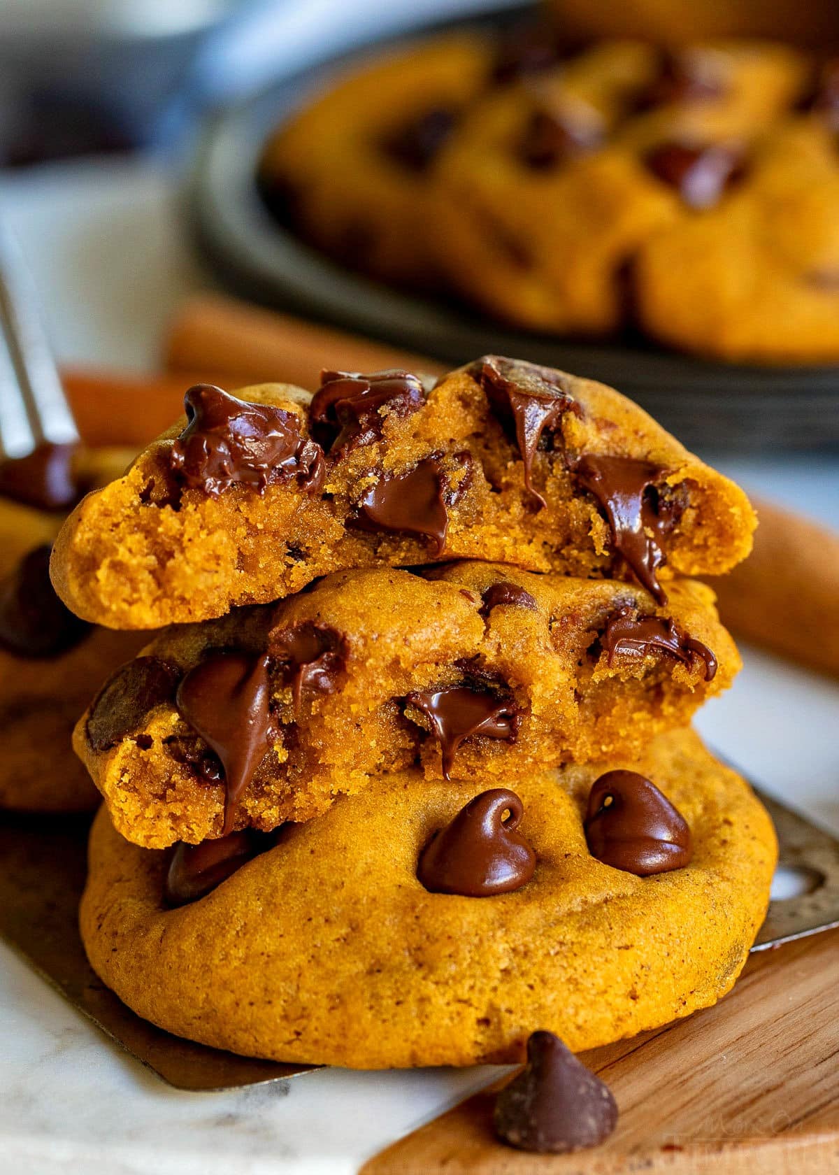 two pumpkin chocolate chip cookies with one of them split in half and stacked on the other. Chocolate chips are still melty.