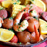 top down view of shrimp boil in serving dish made with shrimp, potatoes, corn and more. shown with lemon wedges for serving.