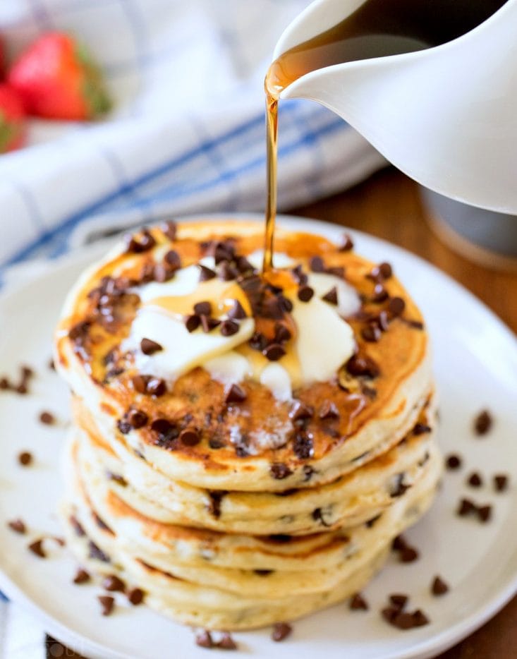 syrup being poured onto a stack of chocolate chip pancakes