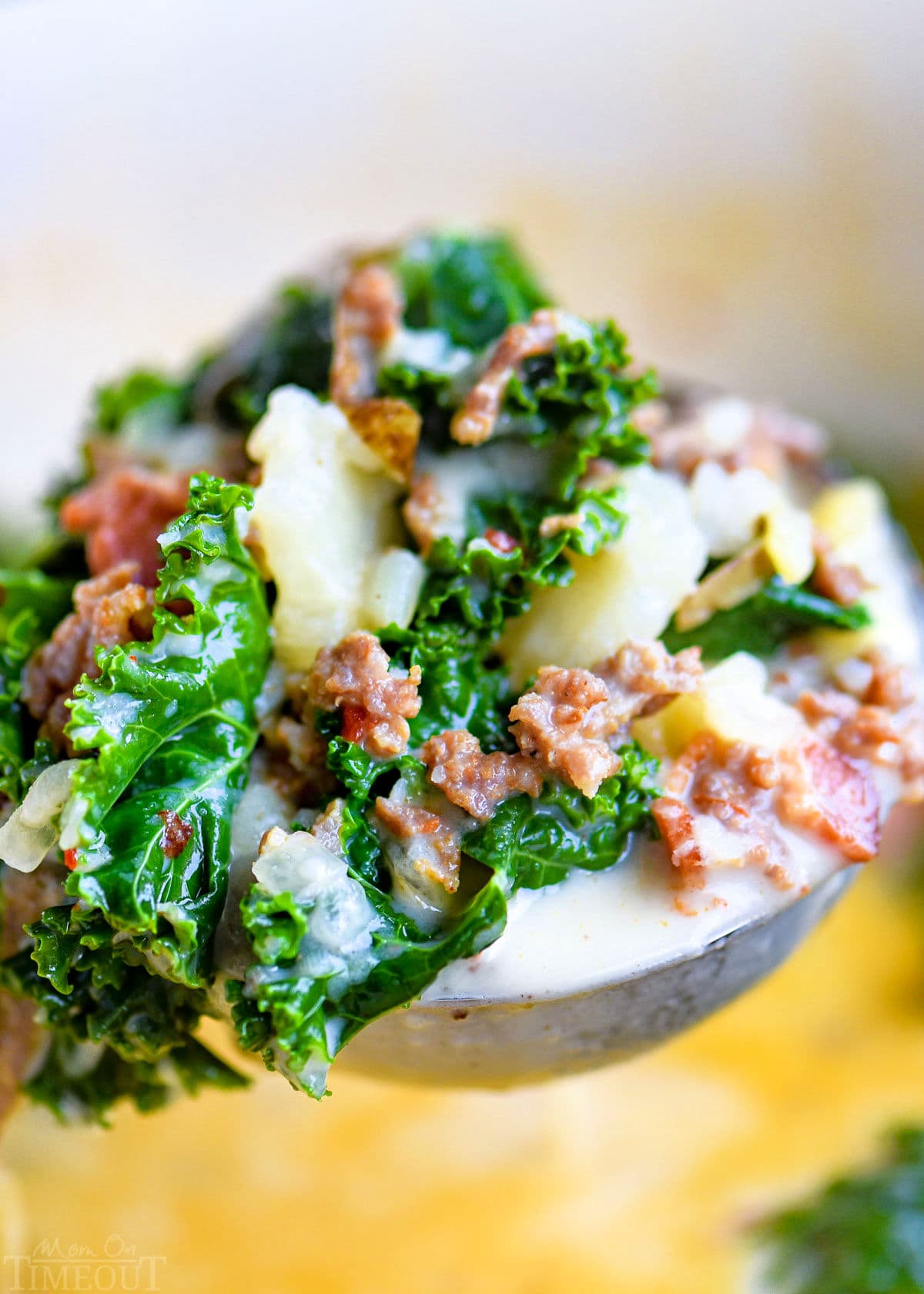 ladle full of soup made with kale, potatoes and sausage held above the pot of soup.