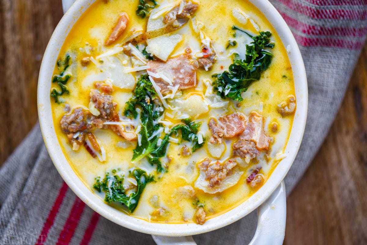 top down view of a bowl of zuppa toscana soup in a white bowl with handles. Soup is topped with Parmesan cheese and is sitting on a brown and red linen napkin.