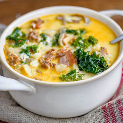 white bowl with handles filled with zuppa toscana soup and topped with cheese. Kale, sausage and bacon can be seen in the soup.