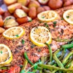 baked salmon with lemon slices on a sheet pan with green beans and red potatoes.