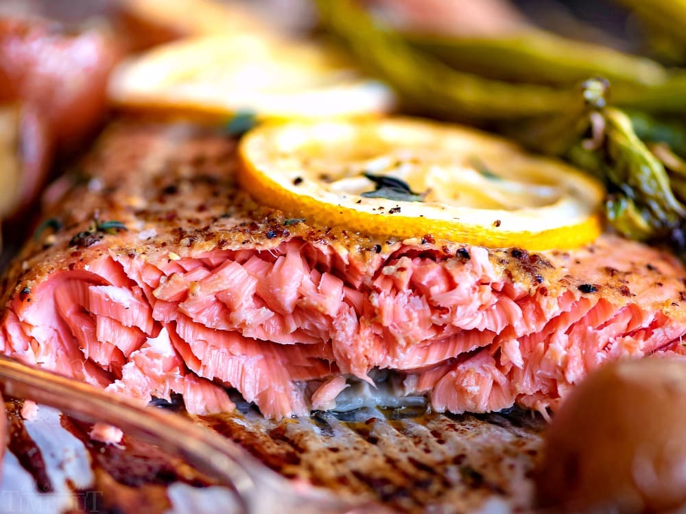 Easy Baked Salmon is healthy, delicious, and FAST! Fresh salmon is topped with a simple honey dijon glaze and baked to perfection. Prepped and cooked in under 30 minutes! // Mom On Timeout #bakedsalmon #salmon #salmonrecipe #easysalmonrecipe #easy #sheetpan #dinner #dinners #30minutemeals #veggies baked salmon recipe close up of tender flaking of salmon