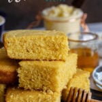 homemade cornbread stacked on a dark cutting board served with honey and butter