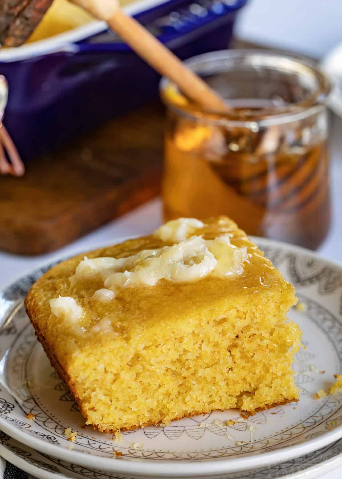 cornbread recipe piece on plate with honey butter and jar of honey in the background