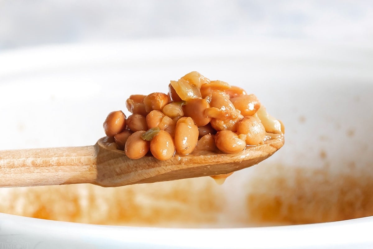 crock pot pinto beans on a wooden spoon held over white crockpot wide shot