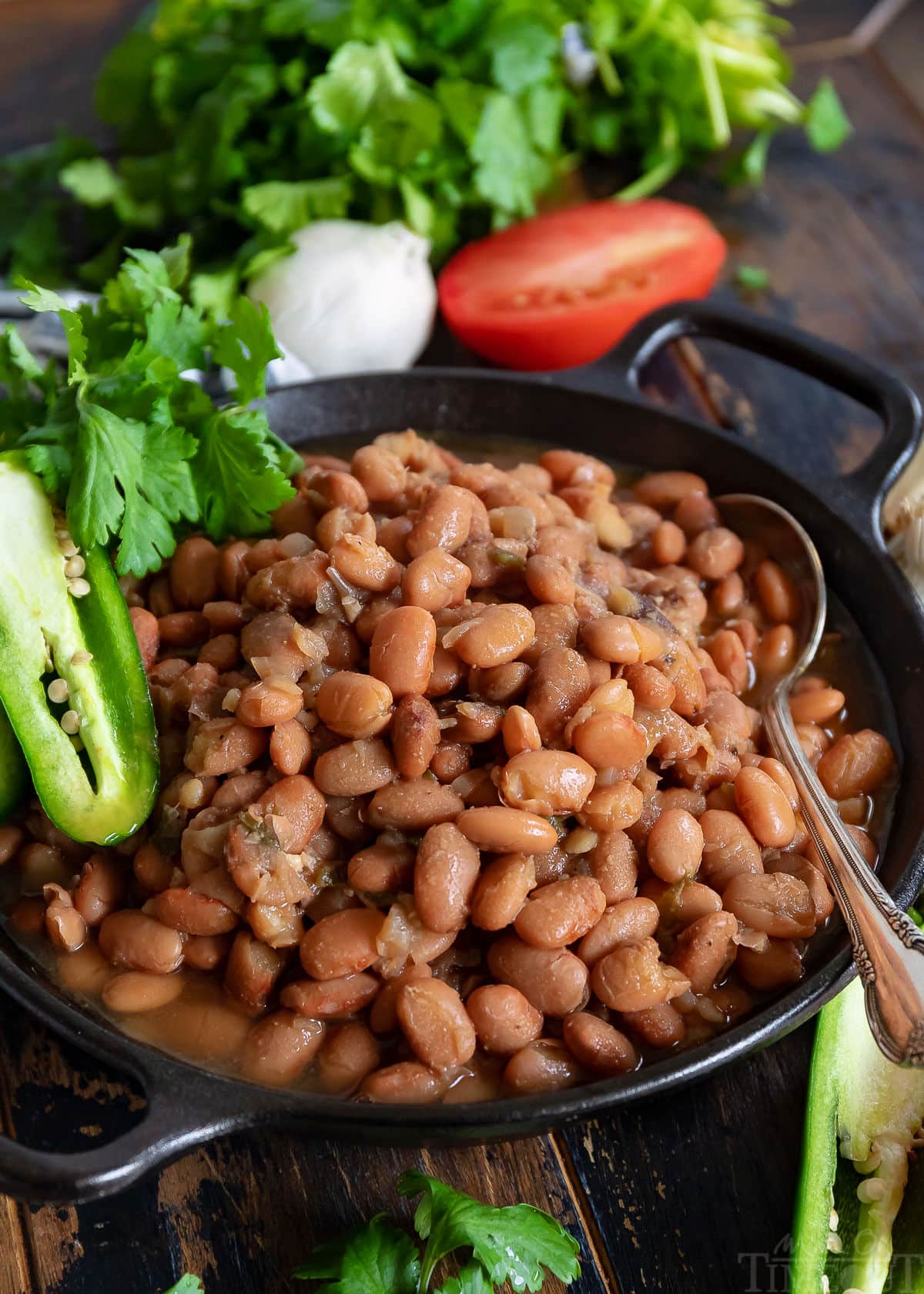 slow cooker pinto beans in black bowl with spoon and garnished with jalapeno tomato and cilantro