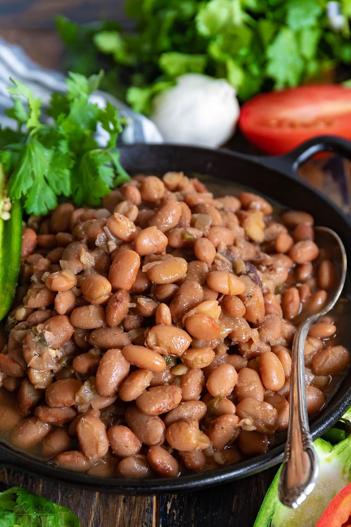 slow cooker pinto beans in black bowl with spoon and garnished with jalapeno and cilantro