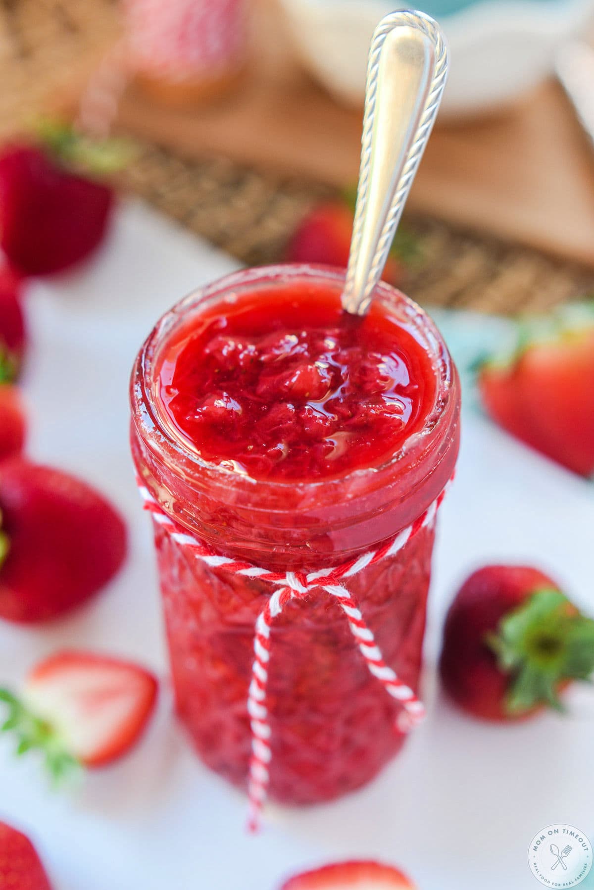 Tall glass jar filled with strawberry sauce for cheesecake or ice cream. Long spoon in the jar for serving.