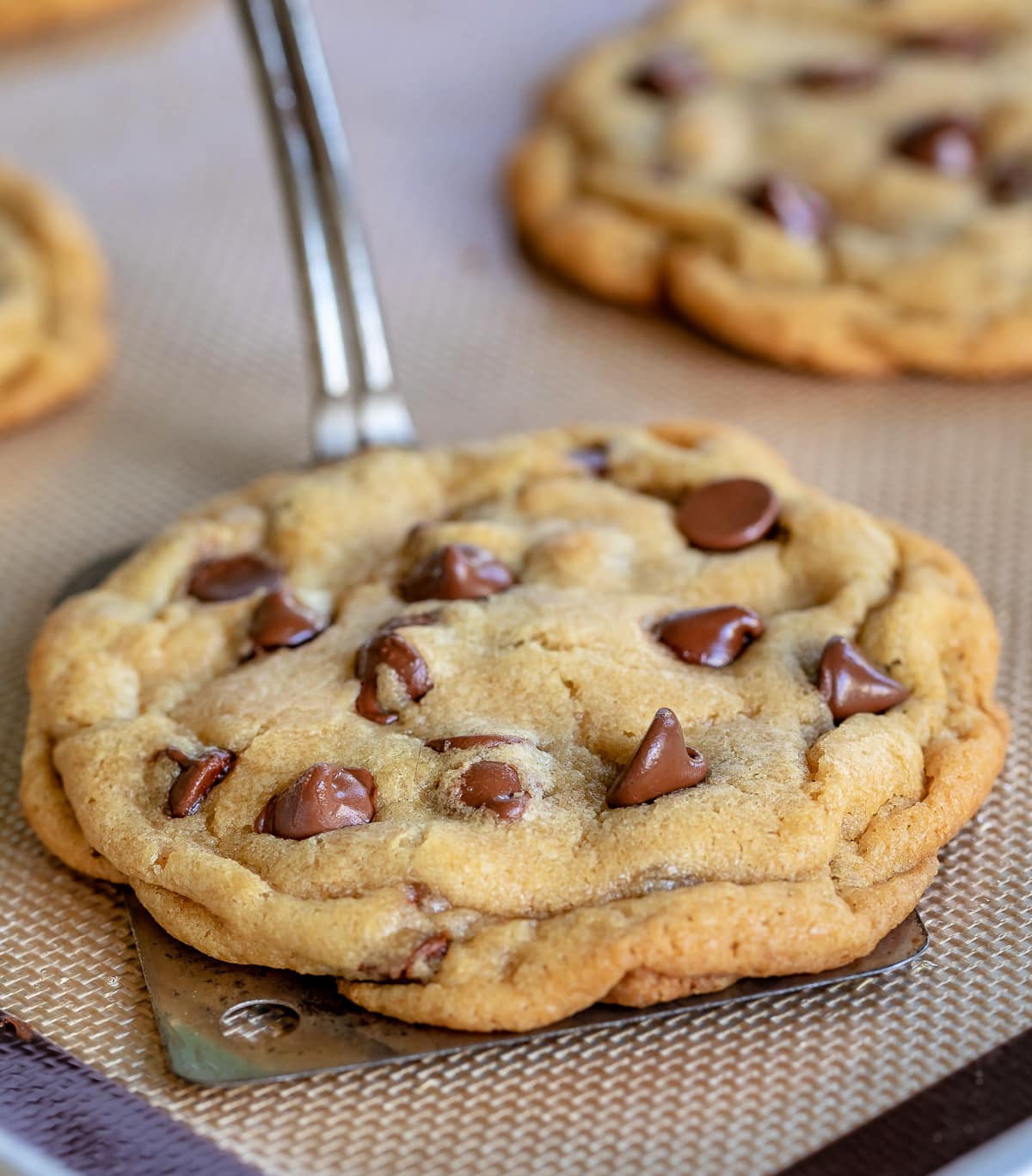 chocolate chip cookie being removed from silicone baking mat with metal spatula 1 shorter