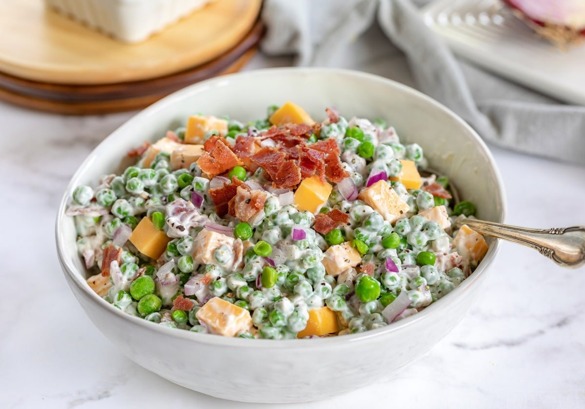 easy pea salad topped with bacon crumbles in large white bowl