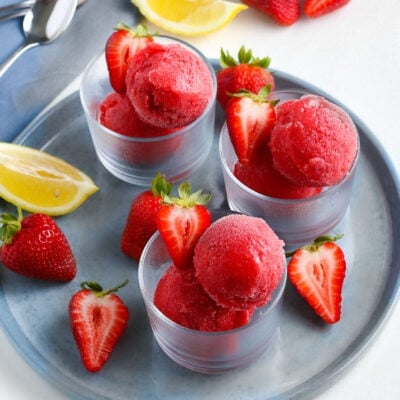 strawberry sorbet in three small glasses on gray plate with halved strawberries as garnish square