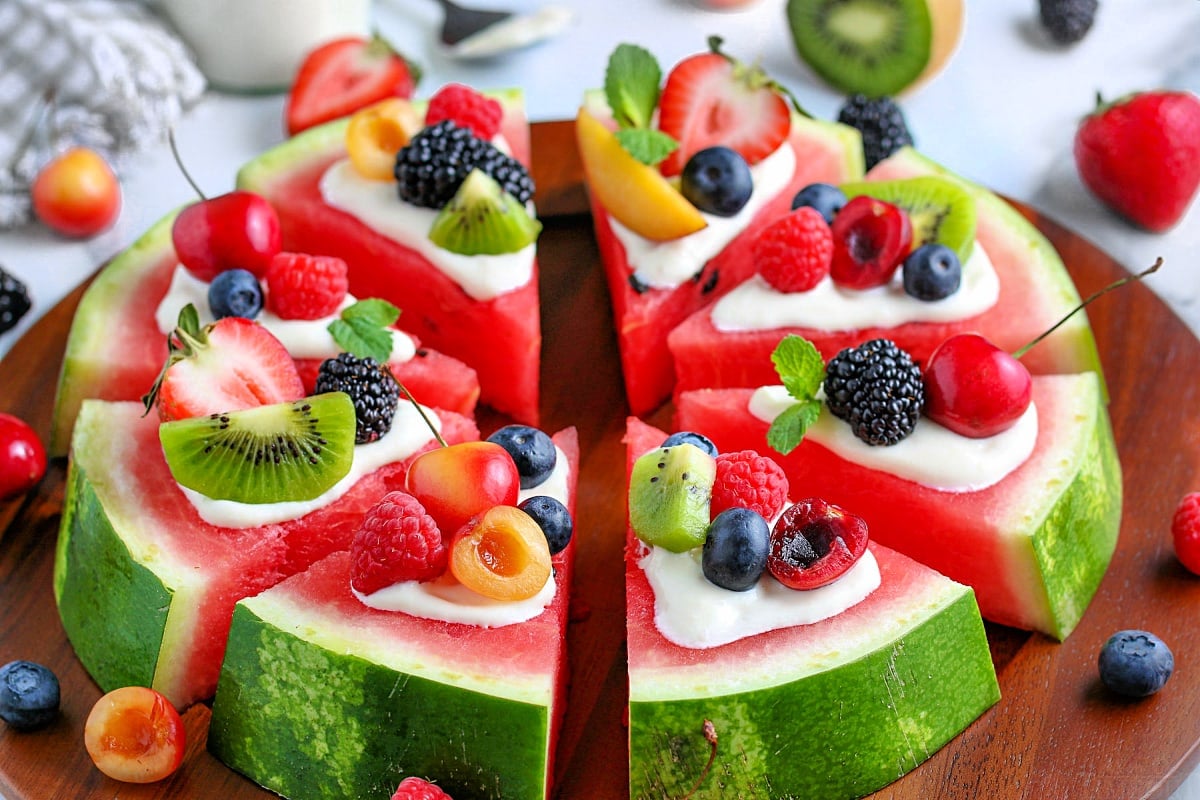 watermelon pizza recipe with a variety of fresh fruit on top cut into wedges on board