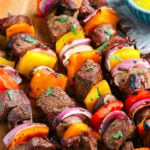 grilled steak kabobs ready to eat on wood plate with text overlay pinterest